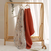 Dog Park swaddle and terra cotta blanket hanging from wooden crib rail in nursery